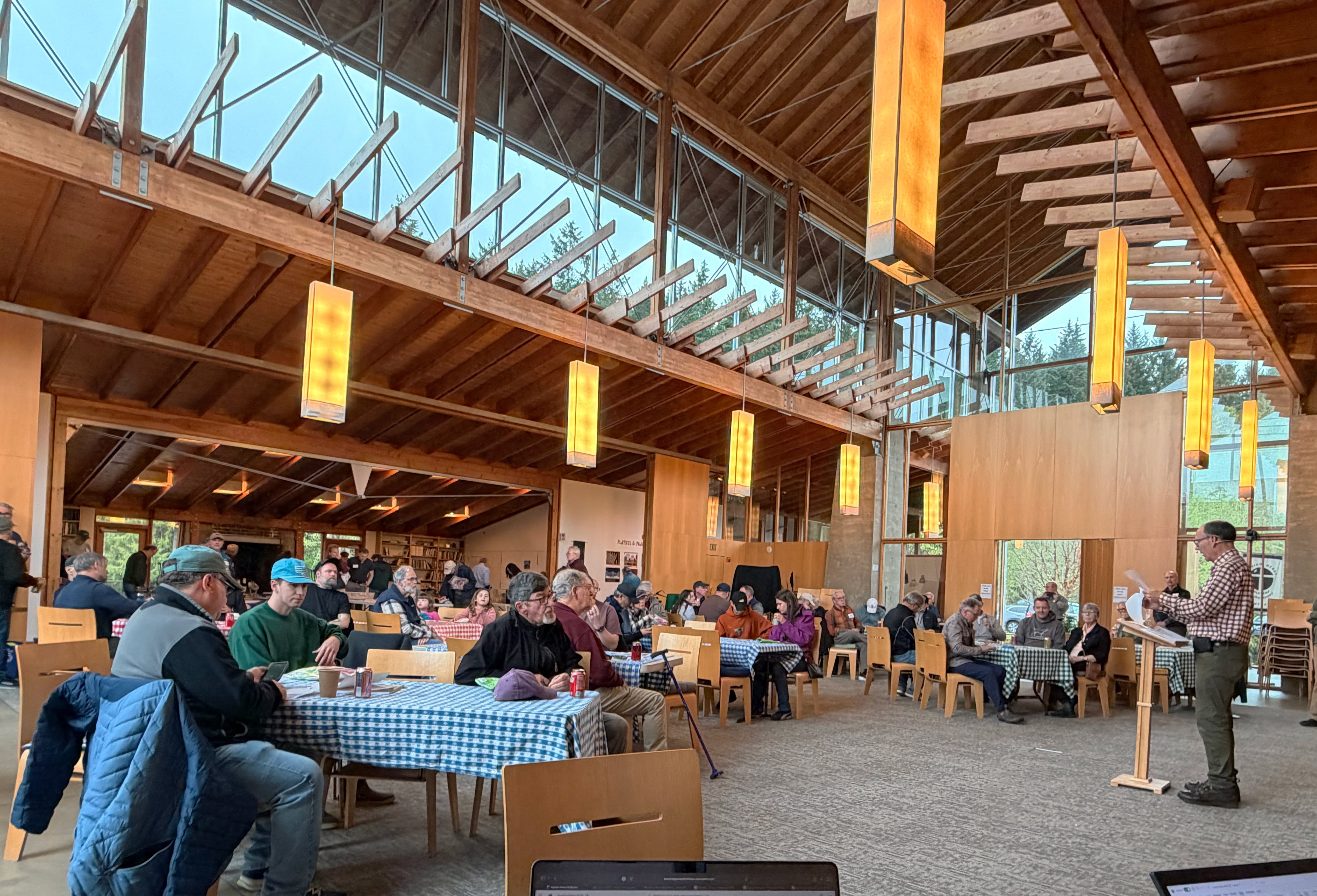 Large gathering of club members at a community hall with wooden beams and skylights